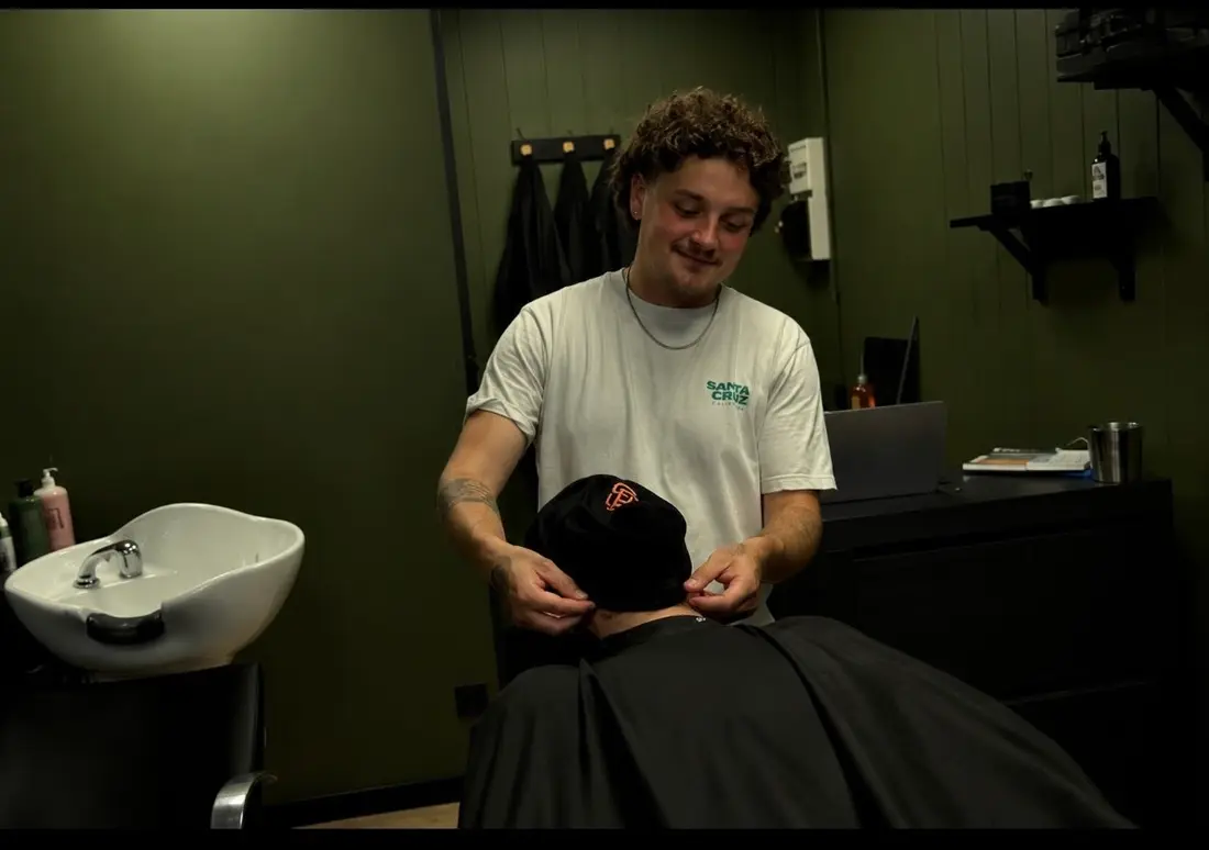 Le barbier ajuste une serviette autour du cou d'un client dans le salon aux murs kaki
